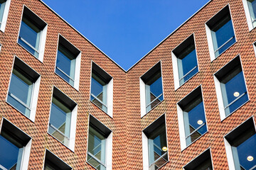 Modern architectural building with geometric design featuring multiple windows and brick facade against a clear blue sky, showcasing contemporary urban aesthetics and structure