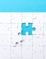 A nearly complete white jigsaw puzzle against a light blue background, with one piece missing and another held separately nearby