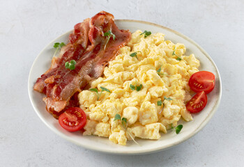 Scrambled eggs with crispy bacon and tomatoes on a white background. Classic breakfast.