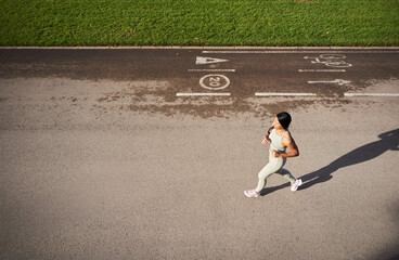 Dynamic top view of african millennial woman jogging on asphalt track in park. Long shadow on pavement adds graphic composition while showing energy, health and active lifestyle.