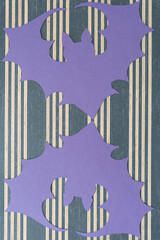 two purple paper silhouettes of bats on striped paper