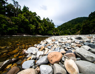 Tranquil Riverbank with Smooth Stones and Lush Greenery