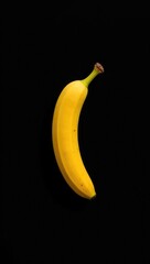 A single ripe yellow banana with a green stem isolated on a solid black background.