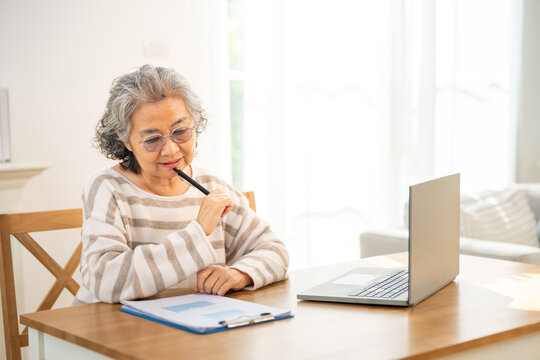 Asian senior woman using laptop computer with internet for e-Learning, household bookkeeping, business financial work at home. Elderly people smart life with technology and digital gadget device.