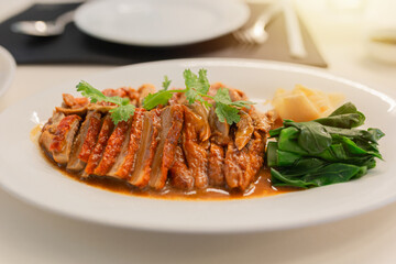 Roasted duck with rich brown sauce served on a white plate, garnished with fresh cilantro, vegetables, and pickled ginger. Asian food culture.