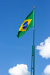 Composição vertical da bandeira do Brasil em um mastro alto contra o céu azul