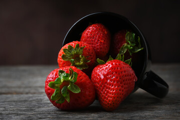 Strawberry Still Life. A black mug on its side with fresh picked strawberries spilling onto a rustic wooedn table.