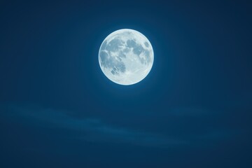 Bright full moon rises above thin clouds in deep blue night sky high detail