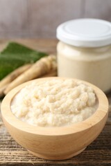 Tasty horseradish sauce and roots on wooden table, closeup
