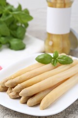 Pickled asparagus spears with basil on grey table, closeup
