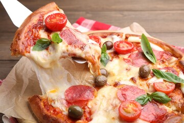 Taking piece of delicious pizza with cheese, salami, tomatoes and olives at table, closeup