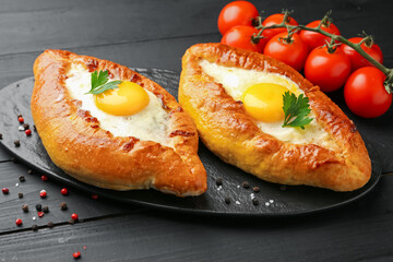 Tasty khachapuri with cheese, eggs, tomatoes and spices on black wooden table, closeup
