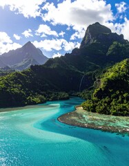 Lush green mountains meet turquoise lagoon, a waterfall cascading down rocky slopes into vibrant, shallow water with a visible sandbar
