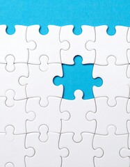 Fototapeta premium A mostly complete white jigsaw puzzle on a blue background with one missing piece in the center