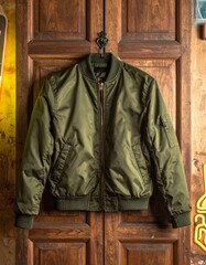 Fototapeta premium Olive green bomber jacket hanging on a wooden door, Casual fashion outerwear displayed indoors