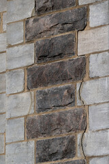 An exterior wall of a building with a large vertical crack. The rough textured wide bricks are both dark grey and light gray. The material is arranged granite tiles with dark in the middle of the wall