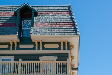 The corner of a hip roof with dark green and red cedar shakes. There's a single inset gable glass window with white trim. The eave of the vintage building is cream color with yellow cornice brackets.  © Dolores  Harvey
