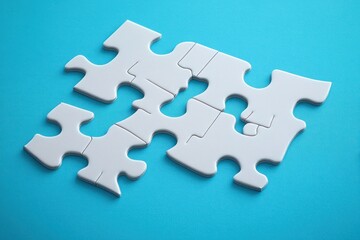 Obraz premium Close-up of partially assembled white jigsaw puzzle pieces on a bright blue surface symbolizing problem solving and connection