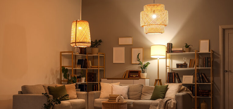 Interior of stylish living room with grey sofas, glowing lamps and bookshelves at evening