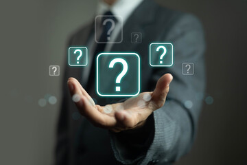 Businessman hand holding digital question mark icons, symbol of doubt, uncertainty, decision making, problem solving, and business challenge concept. Modern solution, consulting and strategy idea.