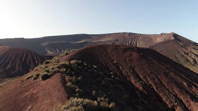 A wide, sweeping shot reveals a desolate cinder cone volcano with sparse, resilient vegetation clinging to its slopes grey, raw, motion