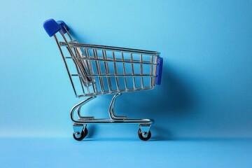 Empty miniature shopping cart with blue handles on a blue background suggesting shopping or consumerism concept