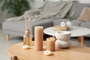 Burning candles, reed diffuser and decor on wooden table in living room
