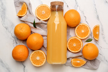 Glass bottle of tasty juice with fresh oranges and napkin on marble background
