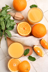 Glasses of tasty juice with oranges, mint leaves and wooden juicer on white tile background