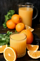 Glass of tasty juice with oranges and mint leaves on dark wooden table
