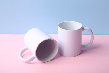 Stylish ceramic mugs on pink table against blue background