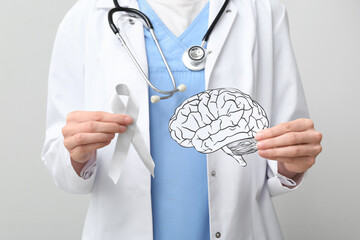 Doctor holding awareness ribbon and paper brain against grey background. Brain cancer concept