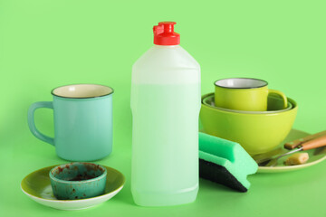 Dirty dishes, detergent and sponge on green background