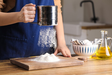 Woman with sieve sifting flour on table in kitchen