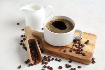 Cup of hot coffee with beans and jug of fresh milk on white background