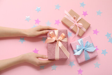Female hands with gift boxes and confetti on pink background