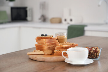 Toasts with tasty peanut butter, nuts and cup of tea on table in kitchen, closeup