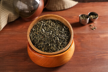 Bowl and strainer with dried green tea leaves on wooden background