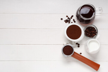 Bowl of coffee powder with beans, portafilter, jugs and sugar cubes on white wooden background