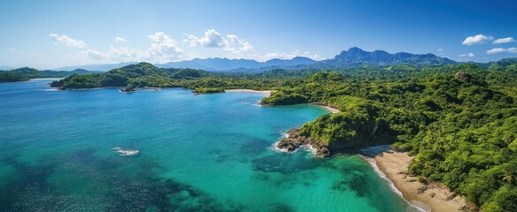 Aerial view of a tropical coastline with turquoise blue water, sandy beaches, lush green forest, and distant mountains under a clear blue sky