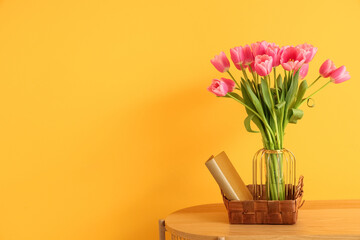 Vase with beautiful tulip flowers and books on wooden bench near orange wall