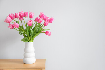 Vase with bouquet of beautiful tulip flowers on table near white wall, closeup