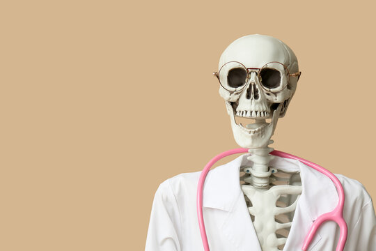 Human skeleton in doctor uniform on beige background