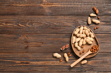 Plate with unpeeled and peeled peanuts on wooden background