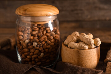 Tray with jar and bowl of peanuts on wooden table, closeup