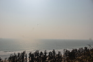 Beautiful panoramic Bangladesh sea view with endless ocean waves reflecting sunlight behind coastal tree forest background.