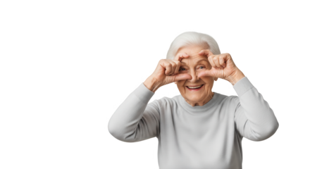 Elderly woman with white hair, smiling and making a heart shape with her hands over her eyes, isolated on transparent background