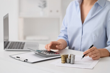 Fototapeta premium Businesswoman with coins using calculator at table in office, closeup. Tax concept