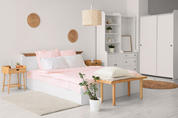 Bed with stylish pink bedding, shelving unit, bedside tables, bench and houseplants in bedroom