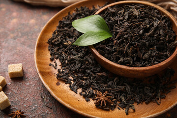 Wooden bowl and plate with dry black tea leaves on dark background, closeup